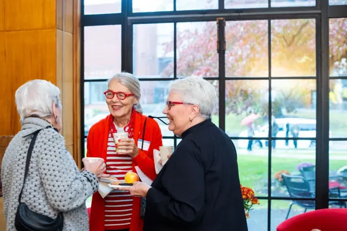 Three alums gathered in the Alumnae House smiling and talking.